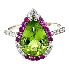 Peridot Diamond and Pink Sapphire White Gold Cocktail Ring  This beautiful ring has a Pear Cut Peridot in the center that weighs 2.77 carats. The ring is surrounded by a cute halo of alternating diamonds and pink sapphires. There are 21 Round Cut Natural Diamonds that weigh 0.31 carats and 14 Pink Sapphires that weigh 0.26 carats. The total carat weight of the ring is 3.34 carats. The diamonds have a clarity of SI and color of F. The setting is crafted in 14K White Gold and weighs 2.9 grams. Thi Green Diamond Ring Pear-shaped, Green Cluster Diamond Ring With Center Stone, Green Cluster Rings With Brilliant Cut, Pear-shaped Green Diamond Ring With Center Stone, Peridot Rings With Brilliant Cut In Fine Jewelry Style, Fine Jewelry Peridot Rings With Brilliant Cut, Green Diamond Halo Ring With Brilliant Cut, Lime Green Diamond Ring With Gemstone, Dazzling Green Rings With Halo Setting