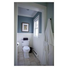 a white toilet sitting next to a window in a bathroom under a framed picture on the wall