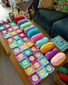 a coffee table with crocheted squares and balls of yarn sitting on top of it