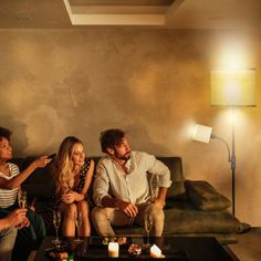 three people sitting on a couch with candles in front of them and one person holding a wine glass