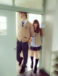 a young man and woman standing in front of a door with their arms around each other