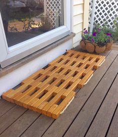 a wooden bench sitting on top of a wooden deck next to a window and potted plants