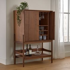 a wooden cabinet with wine glasses and bottles on it in front of a large window