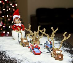 an elf is riding on a toy car in the snow next to a christmas tree