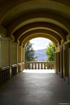 an arched walkway with columns and railings leading to the top of a hill in the distance