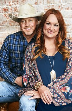 a man and woman sitting next to each other in front of a brick wall wearing cowboy hats