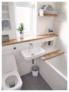 a small bathroom with white tile and wood shelves above the toilet, sink, and bathtub