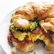 a breakfast sandwich is on a plate with croissants and broccoli