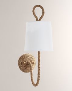 a rope lamp with a white shade hanging from it's side on a wall