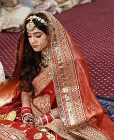 a woman in a red and gold bridal dress sitting on the floor with her hands clasped