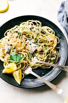 a plate of pasta with meat and parmesan cheese on it next to lemon wedges