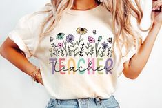 a woman wearing a t - shirt that says teacher with flowers and butterflies on it