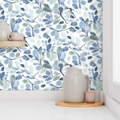 the wallpaper in this kitchen is painted with blue leaves and has white vases next to it