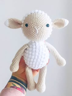 a hand holding a small crocheted sheep in it's left arm,