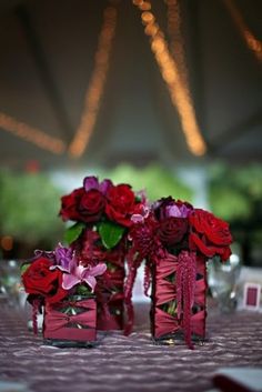 two vases filled with red and pink flowers on top of a table covered in white cloth