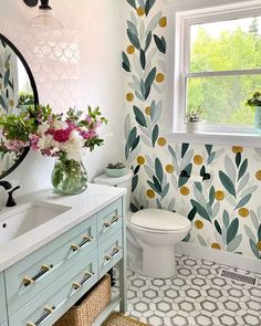 a white toilet sitting next to a bathroom sink under a window with flowers on it