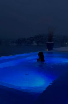 a woman sitting in the middle of a pool at night with blue lights on it