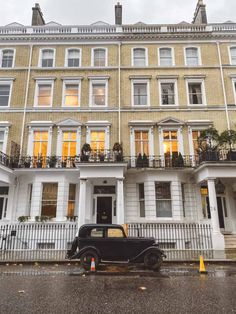 an old black car parked in front of a tall building with balconies on it