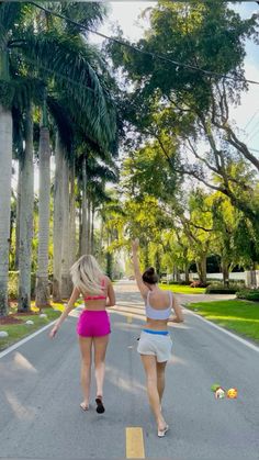 two women walking down the street with their arms in the air and palm trees behind them