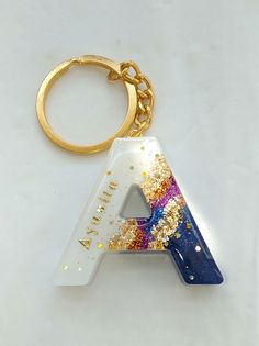 a keychain with the letter a painted in gold and blue glitters on it