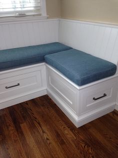 a corner bench with two drawers and a blue cushion on the seat is in front of a window