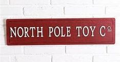 a red sign that says north pole toy co on it's side against a white brick wall