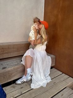 a woman sitting on a wooden bench holding a small child in her lap and kissing her cheek