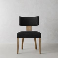 a black chair with wooden legs and backrests in front of a white wall