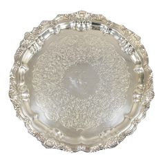 a silver plate with ornate designs on the rim and sides, set against a white background