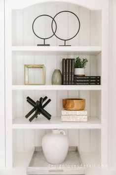 a white book shelf with books and vases on it