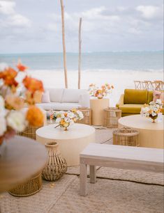 an outdoor seating area on the beach with flowers in vases and chairs around it