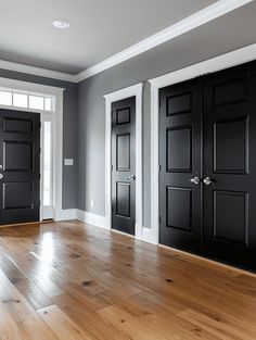 an empty room with three black doors and hard wood flooring on the hardwood floors