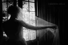 a woman standing in front of a window with a veil on her head and arms behind her back