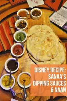 a wooden table topped with lots of different bowls and sauces next to an uncooked pita bread