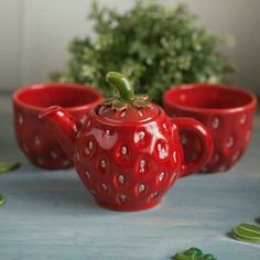 three red ceramic cups and a strawberry shaped teapot