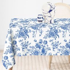 a blue and white table cloth with flowers on it, next to a vase that is sitting on a chair