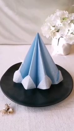 a blue paper cone sitting on top of a black plate next to a vase with white flowers