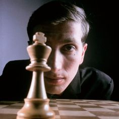 a man sitting at a table next to a chess board with a piece on it