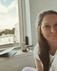 a woman sitting in front of a window smiling at the camera