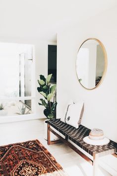 a room with a bench, mirror and potted plant on the floor in front of it