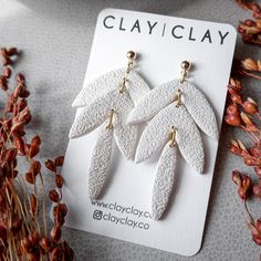 three pairs of white leaf shaped earrings sitting on top of a card next to dried flowers