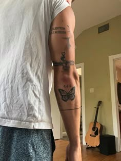 a man with a tattoo on his arm standing in a living room next to a guitar