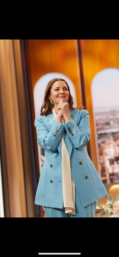 a woman standing in front of a window with her hands clasped