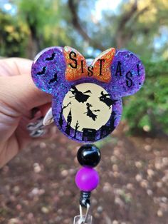 a hand holding up a purple and black mickey mouse head with the word sista on it