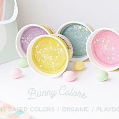 three bowls filled with different colored powders on top of a white table next to candy