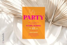 an orange and pink party card on top of a white plate next to palm leaves