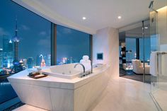 a bathroom with a large bathtub next to a window overlooking the city at night