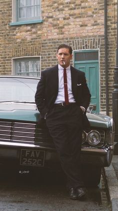 a man in a suit leaning on the hood of a car