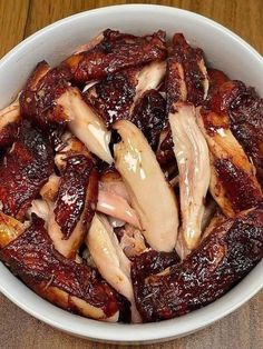 a white bowl filled with meat on top of a wooden table