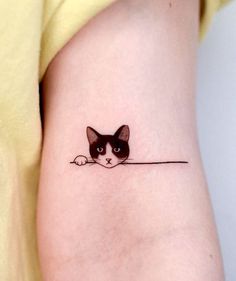 a small black and white cat tattoo on the left side of the arm, with a line drawn across it